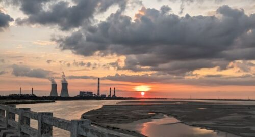 Dramatic sunset view over Raipur's industrial landscape with clouds and a tranquil river.