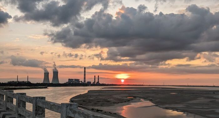 Dramatic sunset view over Raipur's industrial landscape with clouds and a tranquil river.